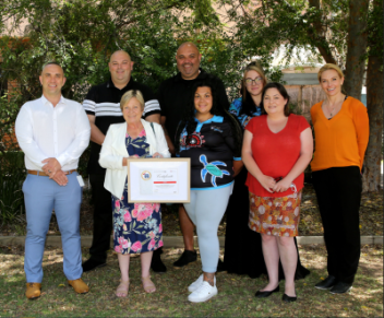 8 people smiling with a certificate standing outside