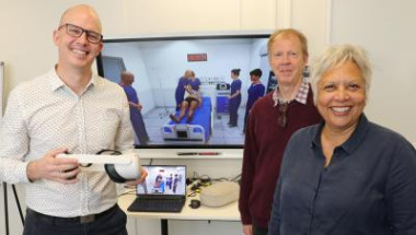 Team photo of 3 people standing in front of TV showing virtual reality education for clinicians